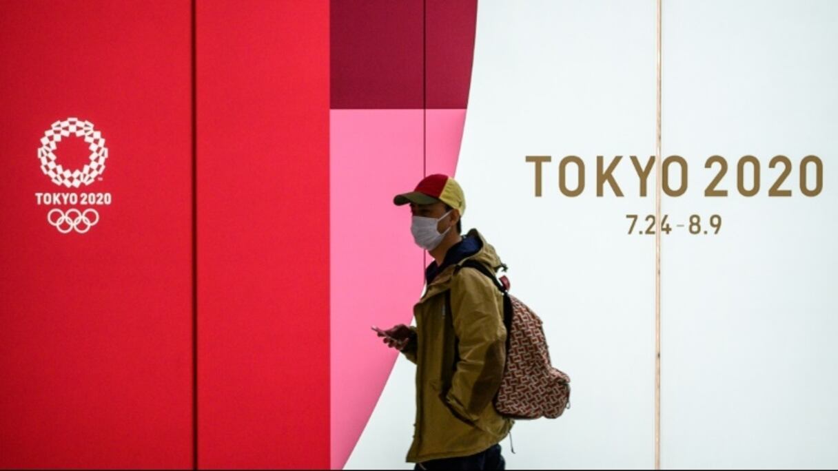 Un homme portant un masque dans le métro passe devant une affiche des Jeux olympiques Tokyo 2020 le 11 mars 2020 à Tokyo.